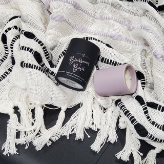 Earth & Ember 'Blackberries & Basil' candle with canister laying on a fringed blanket