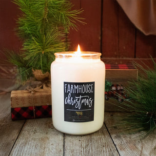 Candle labeled 'Farmhouse Christmas' on a wooden surface with holiday decorations in the background