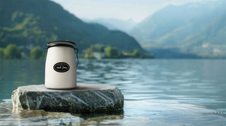 22 oz candle labeled 'North Shore' with a black metal handle and lid sitting on a rock in a body of water