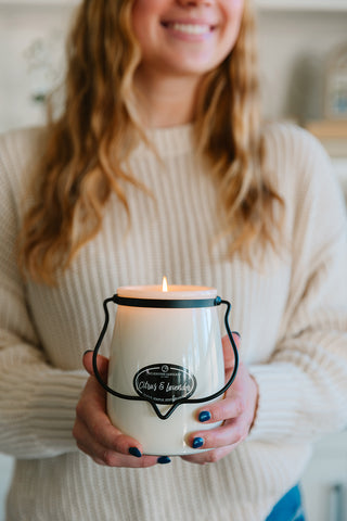 A person holding a lit 22 oz candle labeled 'Citrus & Lavender' wearing a cream colored shirt as the background