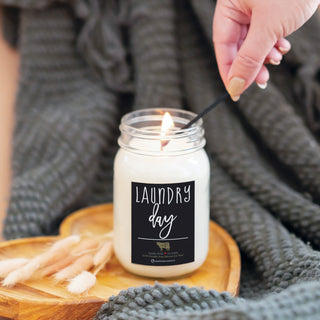 Candle labeled 'Laundry Day' being lit with a wooden board and gray blanket the background