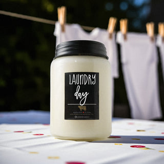 Candle labeled 'Laundry day' on a colorful surface with clothespins and white fabric in the background