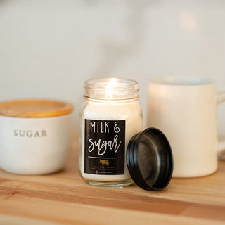 Candle labeled 'Milk & Sugar' on a wooden surface with a mug and sugar in the background