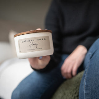 Person holding a 10 oz candle labeled 'Oatmeal, Milk & Honey' in a casual setting
