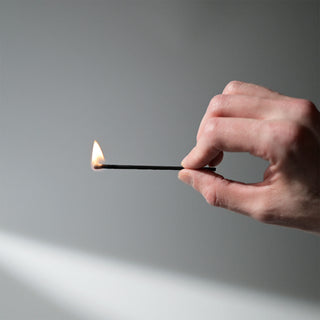 A hand holding a lit match against a white background