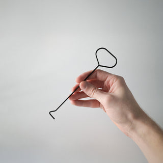 A hand holding a black metal wick dipper against a white background