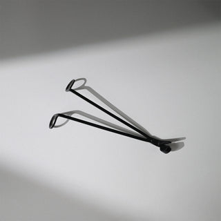 A black metal wick trimmer with a shadow against a white background