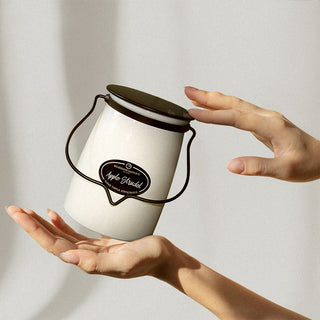 22 oz candle with a black metal handle, labeled 'Apple Strudel' being held in a hand against a white background