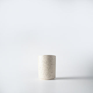 A cream speckled votive sized container against a white background