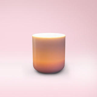 Light pink glass container with a lit candle against a light pink background