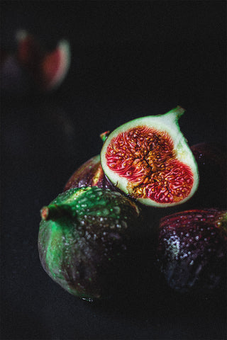 A close-up of a fig cut in half and whole figs in the background