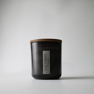 A black glass candle jar with a wooden lid against a white background