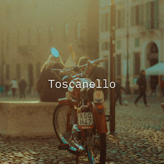 An Italian city with a motor bike in front of a sitting couple with 'Toscanello' in white text overlay