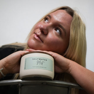 Person holding a 10 oz candle labeled 'Saltwater Mist' against a neutral background