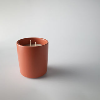 Candle in a burnt orange colored container against a white background