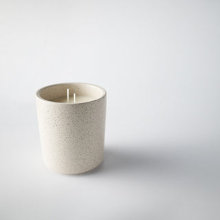 Candle in a cream colored container with speckles against a white background