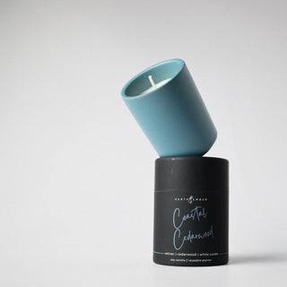 Candle in a dusty blue colored container with a holder labeled 'Coastal Cedarwood' against a white background