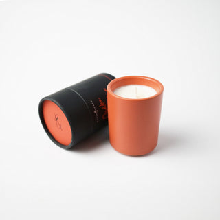 Candle in a burnt orange colored container and holder against a white background