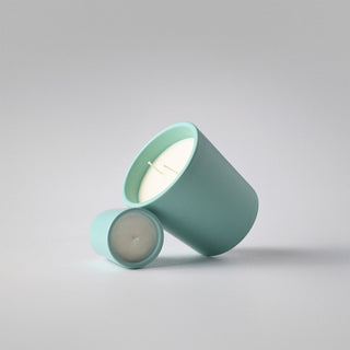 Two seafoam green ceramic containers containing candles against a white background