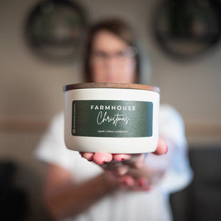 Person holding a 10 oz 'Farmhouse Christmas' candle with a blurred background