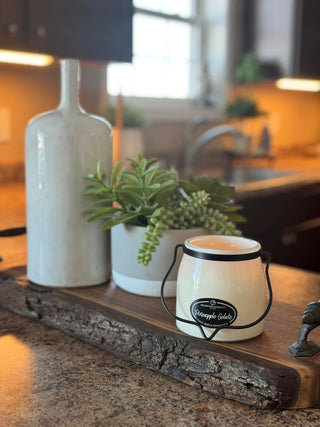 Decorative setup with a white ceramic jar, plant, and decorative item on a wooden surface.